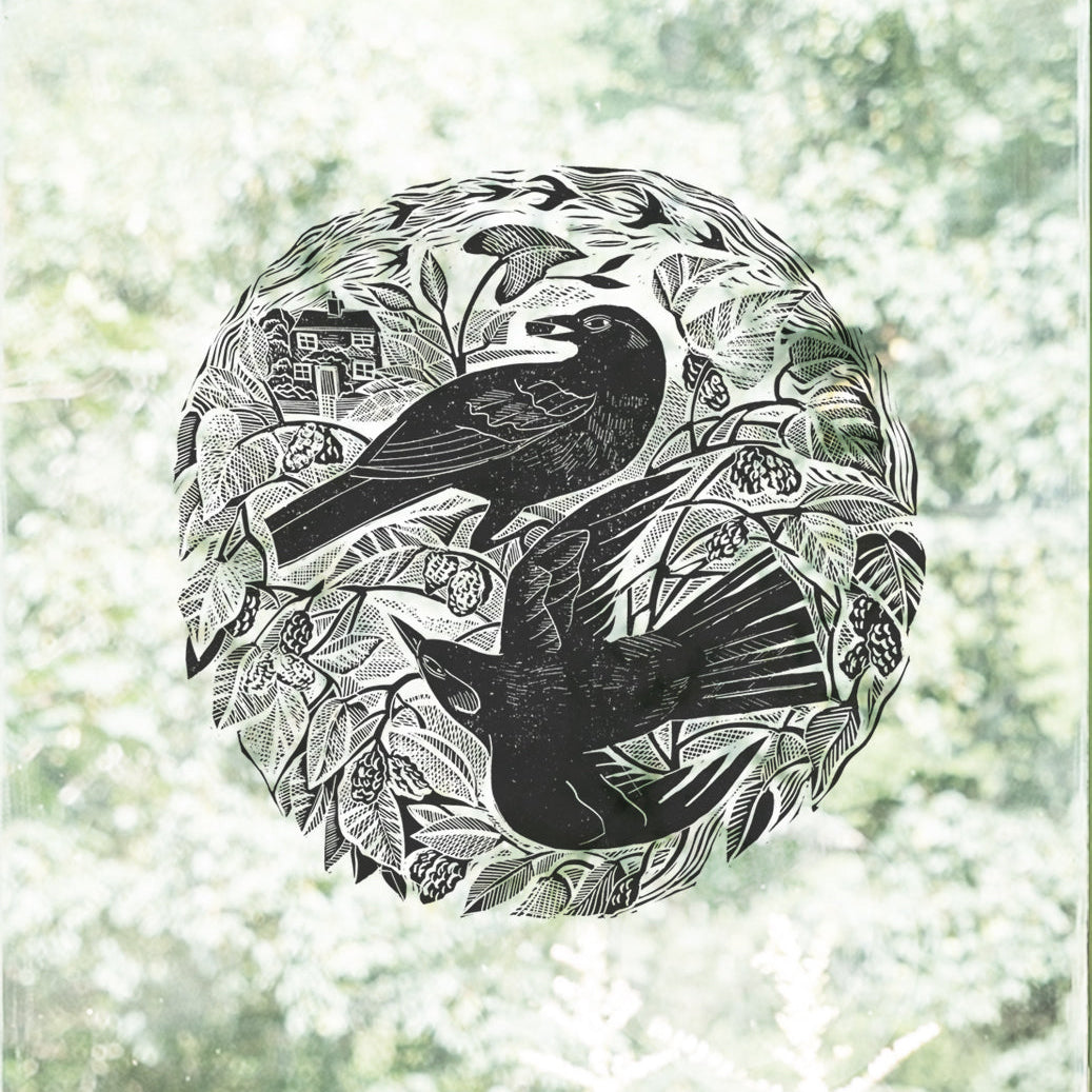 A circular black-and-white linocut or woodcut-style decal by Angela Harding featuring two blackbirds among a mulberry tree