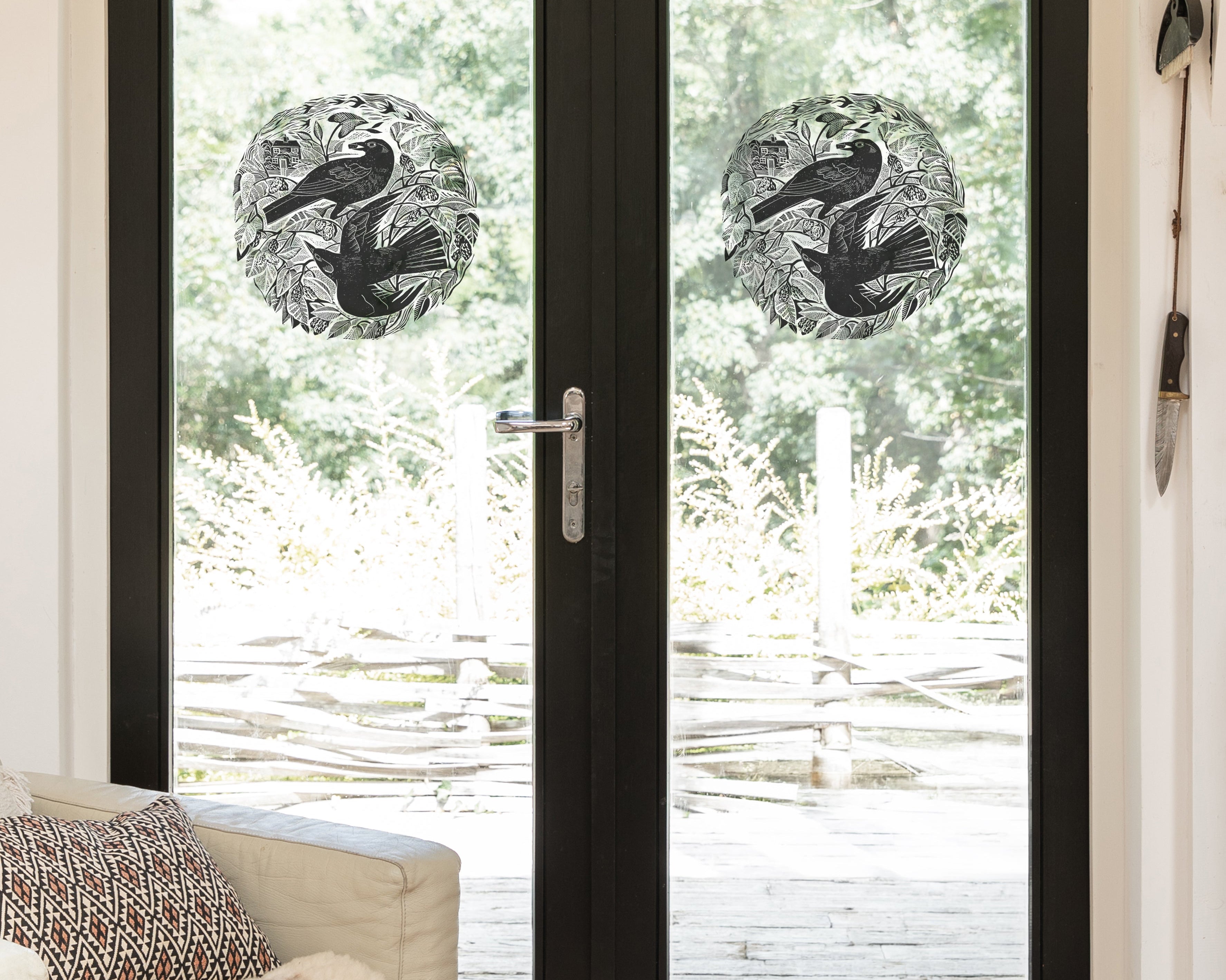Circular black-and-white bird decals on glass doors  shown in a bright room with a light-colored armchair and outdoor greenery visible beyond.