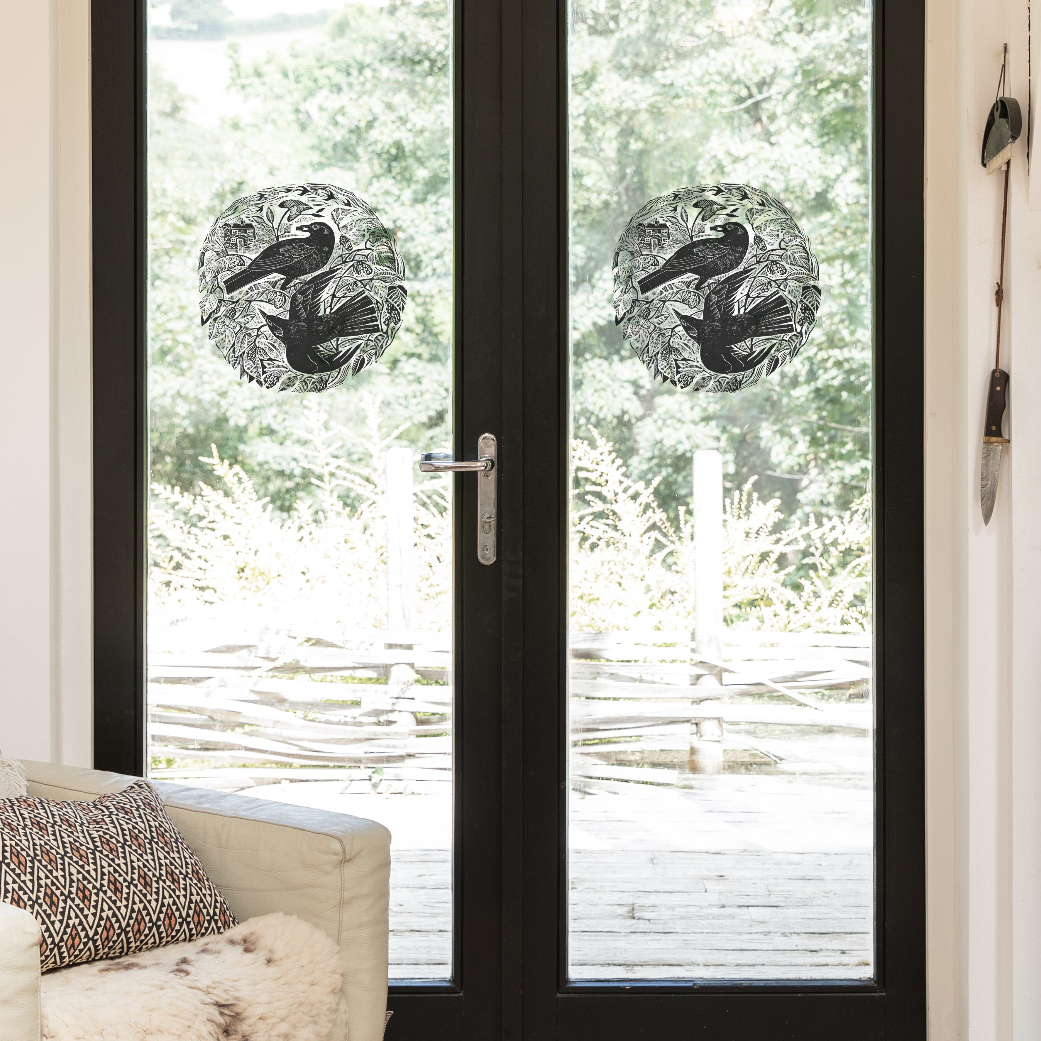 Circular black-and-white bird decals on glass doors  shown in a bright room with a light-colored armchair and outdoor greenery visible beyond.
