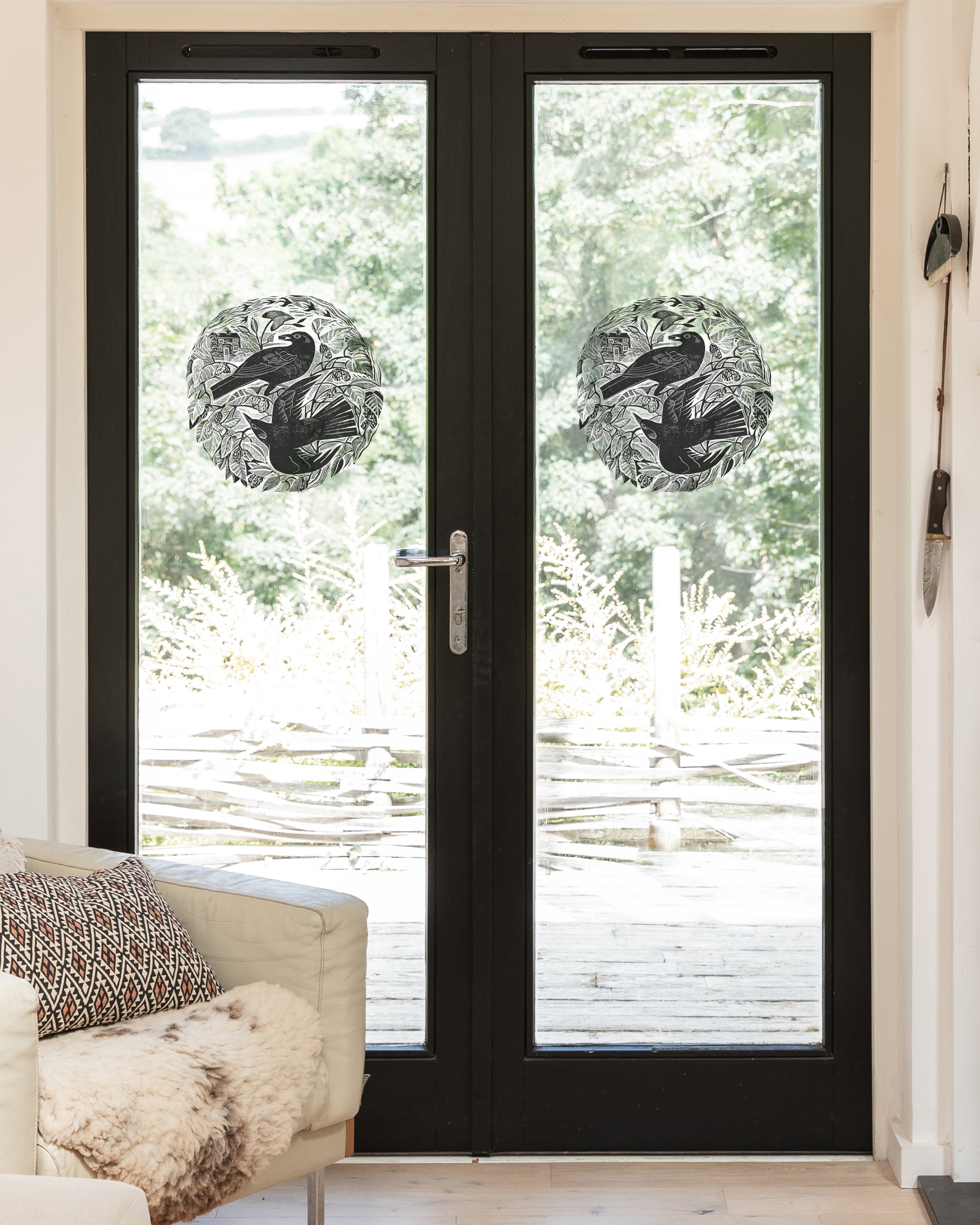 Circular black-and-white bird decals on glass doors  shown in a bright room with a light-colored armchair and outdoor greenery visible beyond.